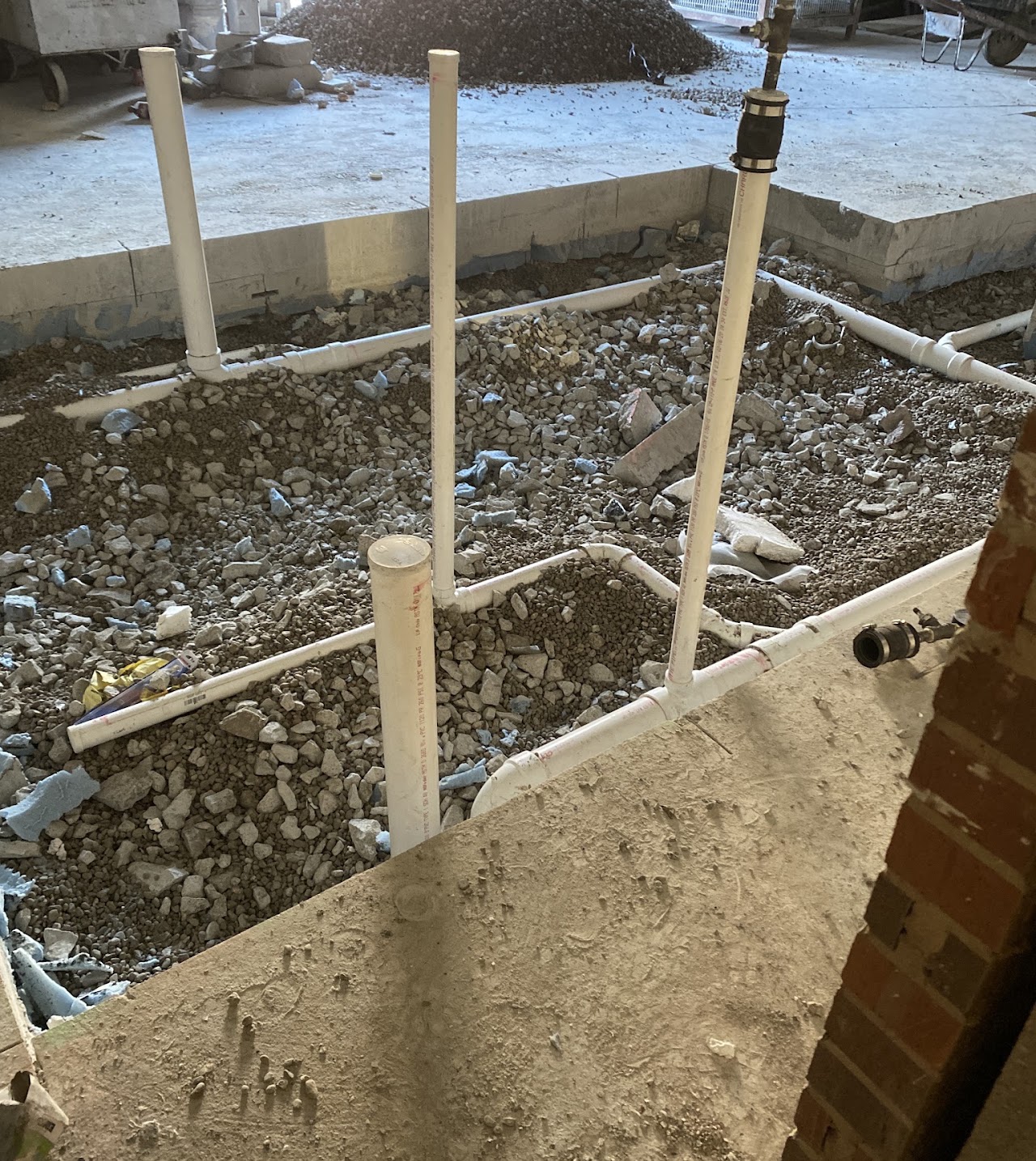 Drain piping and vertical stub-outs exposed through an opened concrete floor